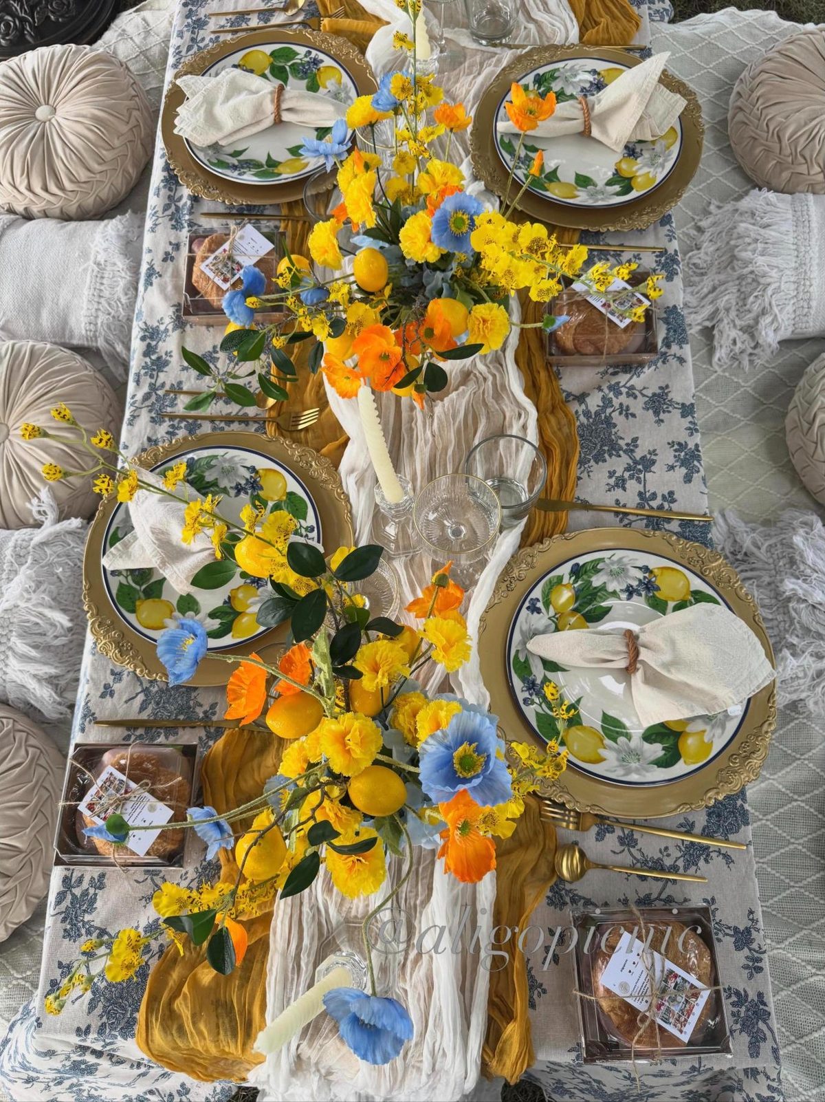 A table seen from above with lemon print plates, blue toile linen, poppies and a saffron runner